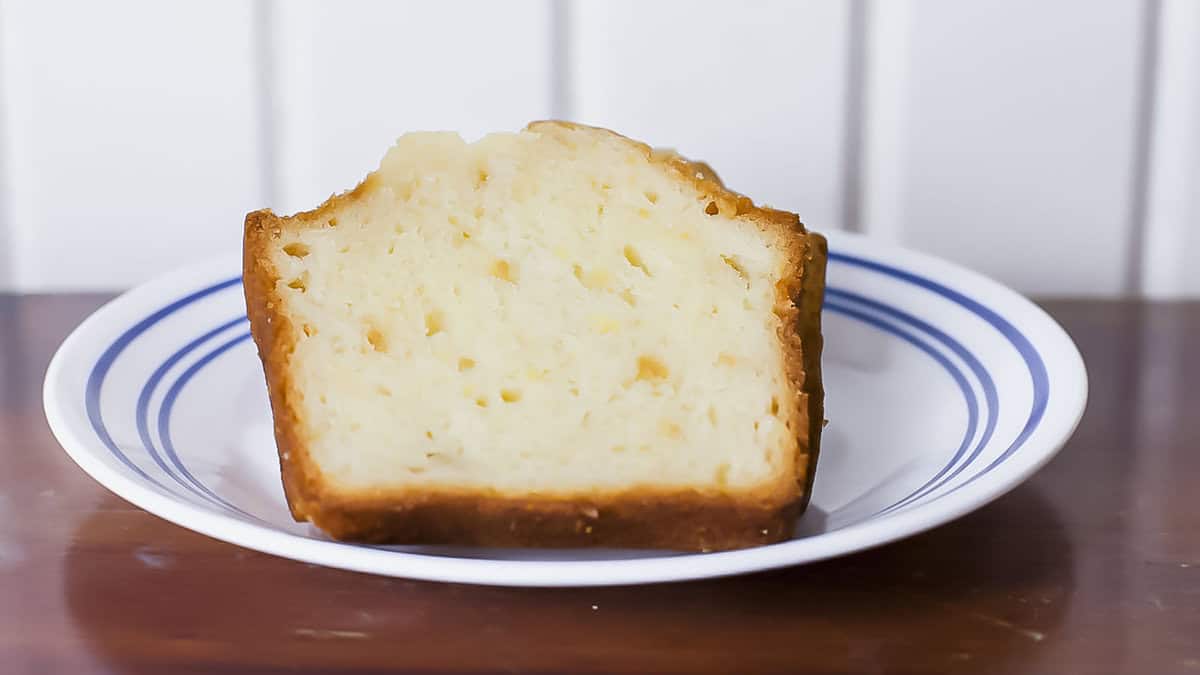 A slice of lemon pound cake on a white plate with blue stripes, placed on a wooden table.