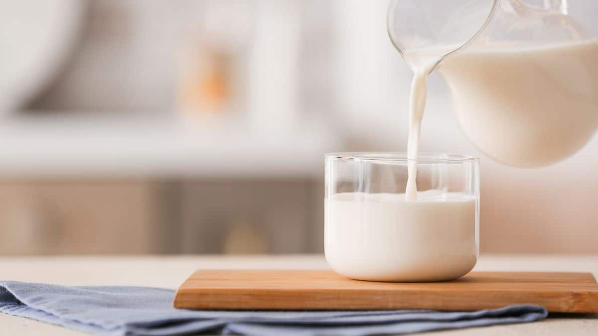 Pouring milk into a glass on a wooden board with a soft-focus background.