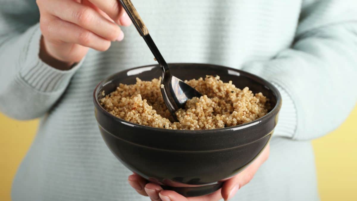 A person holding a black bowl full of cooked quinoa with a fork, wearing a light blue sweater.