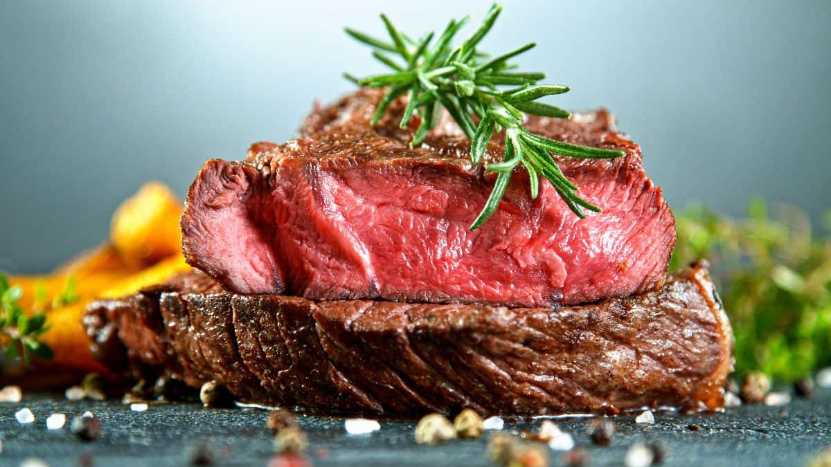 Medium-rare steak garnished with rosemary, served with sliced oranges and seasonings on a slate plate.