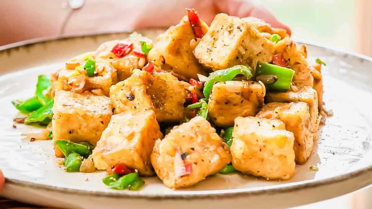 A plate of sautéed tofu cubes with red peppers and green veggies, garnished with herbs.