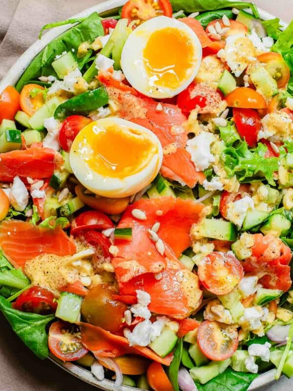 A colorful salad with smoked salmon, halved boiled egg, cucumbers, tomatoes, and mixed greens, sprinkled with seeds.