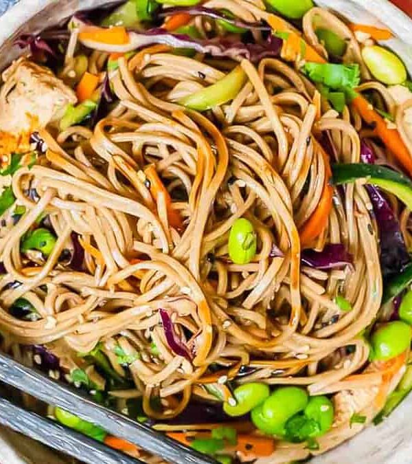 A bowl of stir-fried noodles with vegetables and edamame, ready to be served.