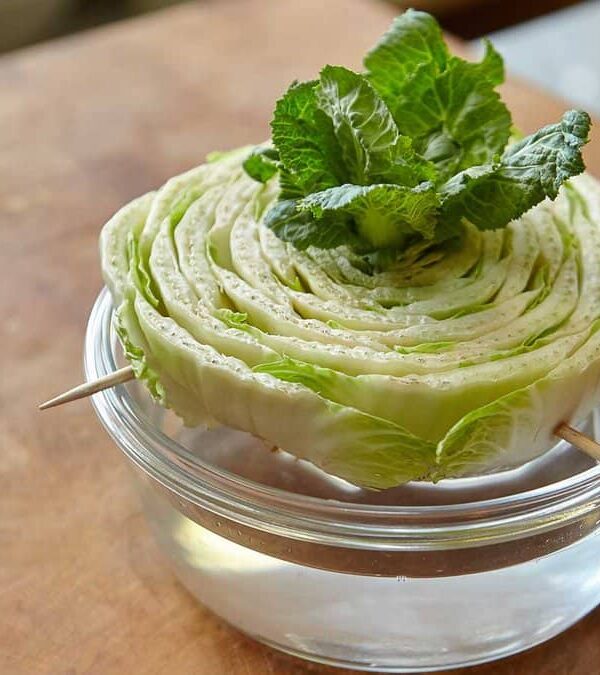 A halved iceberg lettuce with mint leaves on top, secured by toothpicks and placed in a glass bowl on a wooden table.
