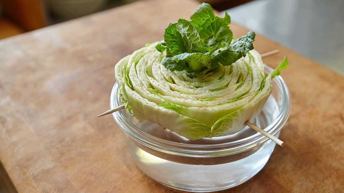 A halved iceberg lettuce with mint leaves on top, secured by toothpicks and placed in a glass bowl on a wooden table.
