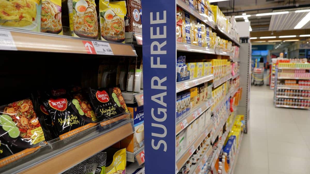 Aisle in a supermarket displaying various sugar-free products, with a prominent blue "sugar free" banner hanging from the ceiling.