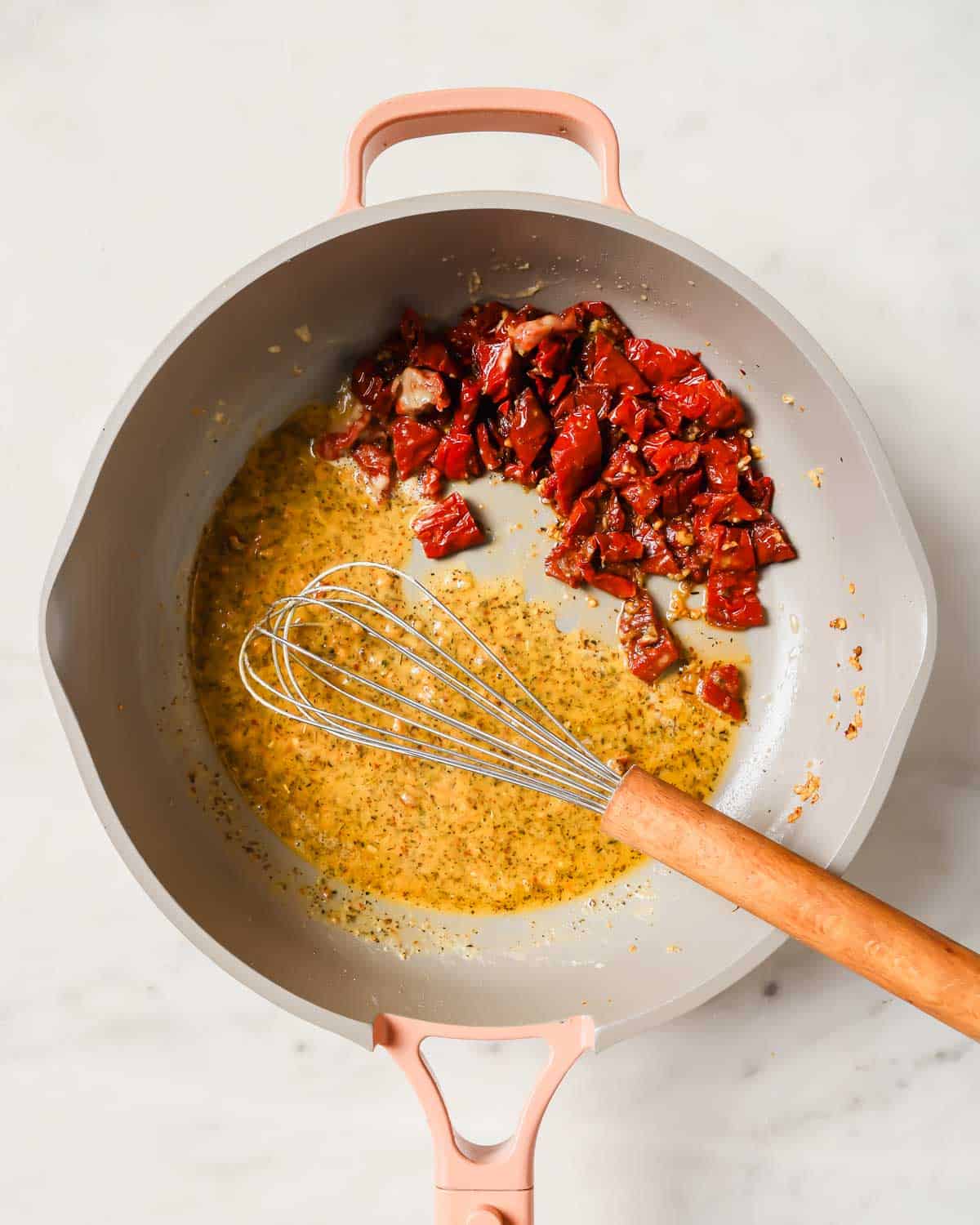 Whisk in a pan with a creamy sauce and chopped sun-dried tomatoes on one side.