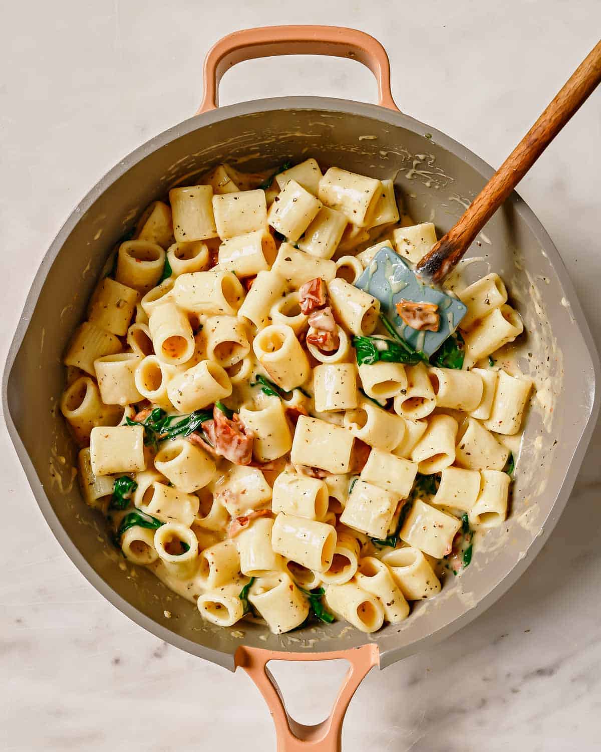 Cooked pasta with spinach and tomatoes in a pot with a wooden spoon.