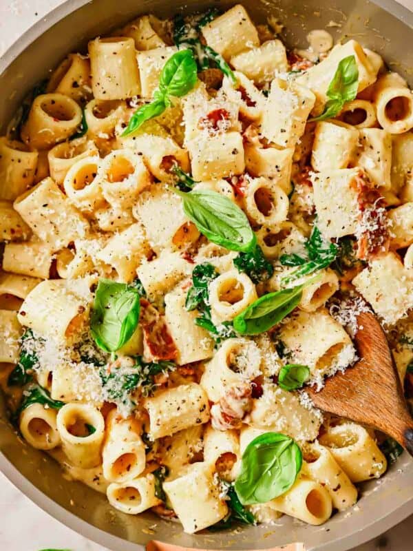 A bowl of rigatoni pasta with parmesan cheese, basil, and wooden spoon.