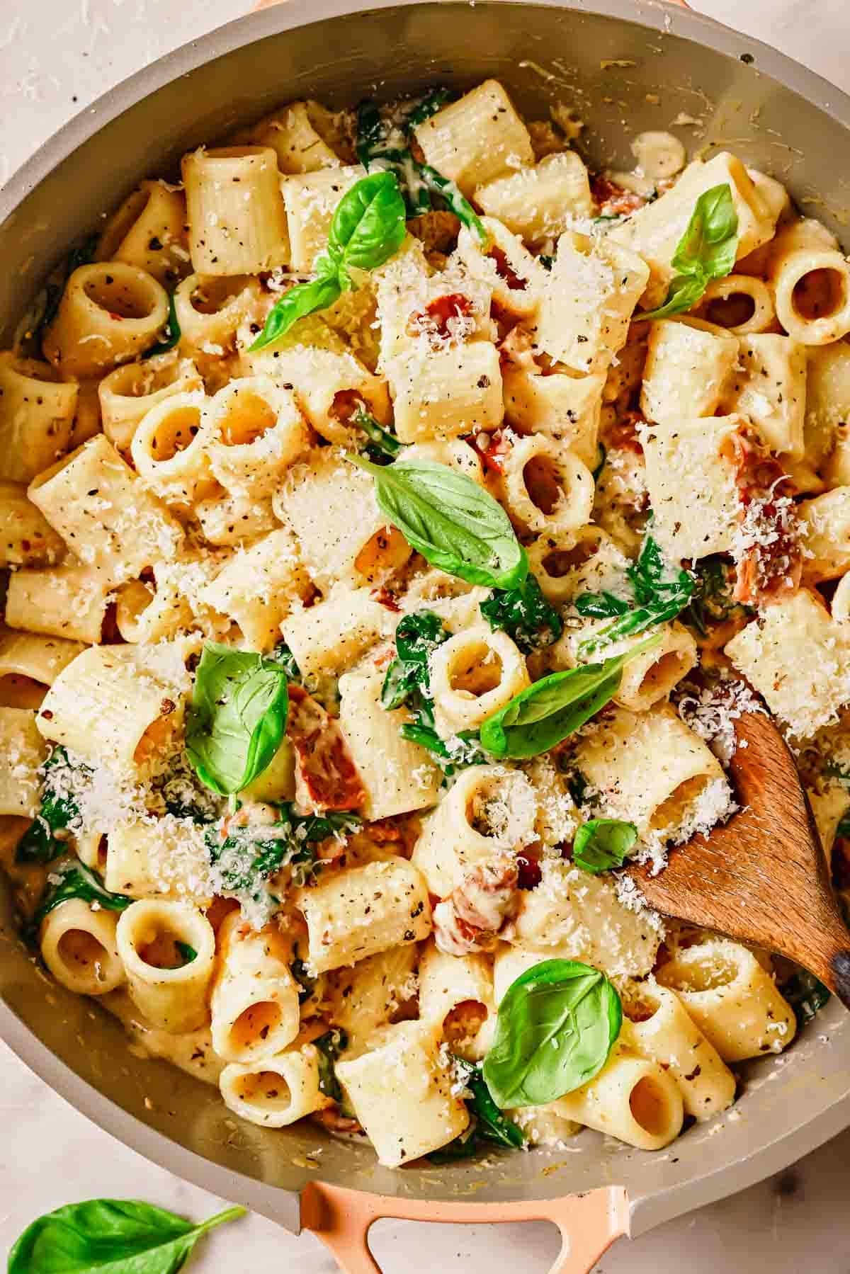 A bowl of rigatoni pasta with parmesan cheese, basil, and wooden spoon.