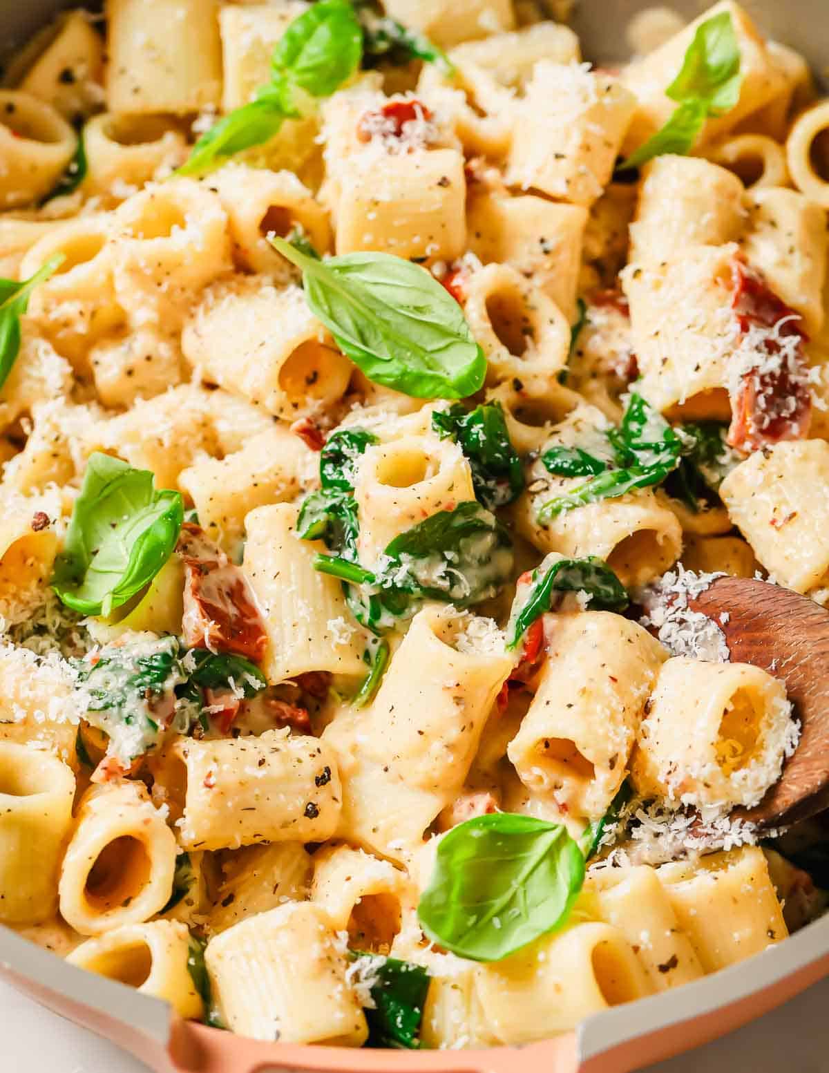 Creamy pasta tossed with spinach, sun-dried tomatoes, and garnished with basil and grated cheese.