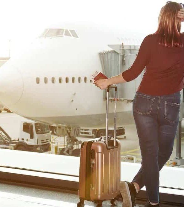 Woman with luggage looking at airplane through airport window, conveying anticipation or travel readiness.