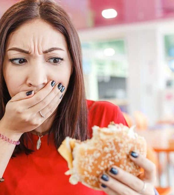 Woman looking at a burger with a disgusted expression while covering her mouth with her hand.