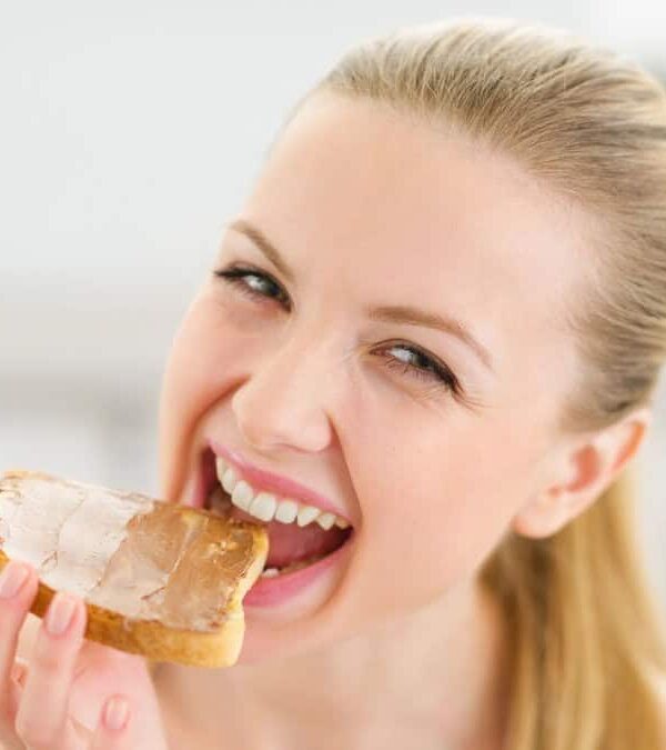 Woman eating a piece of bread with peanut butter.