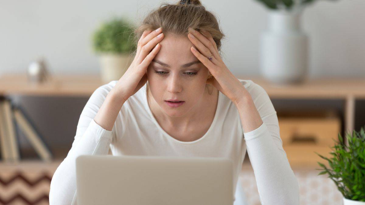 Young woman looking stressed while using a laptop at a desk.
