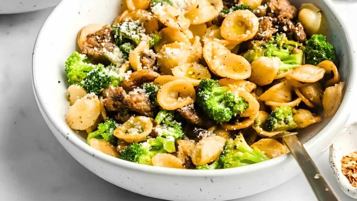 Orecchiette with sausage and broccoli in a white bowl with a serving spoon.