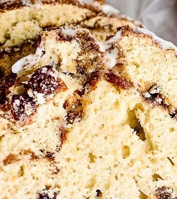 Close-up of two slices of cinnamon raisin bread, featuring a moist, light crumb with visible swirls of cinnamon and sprinkled with a light layer of powdered sugar.