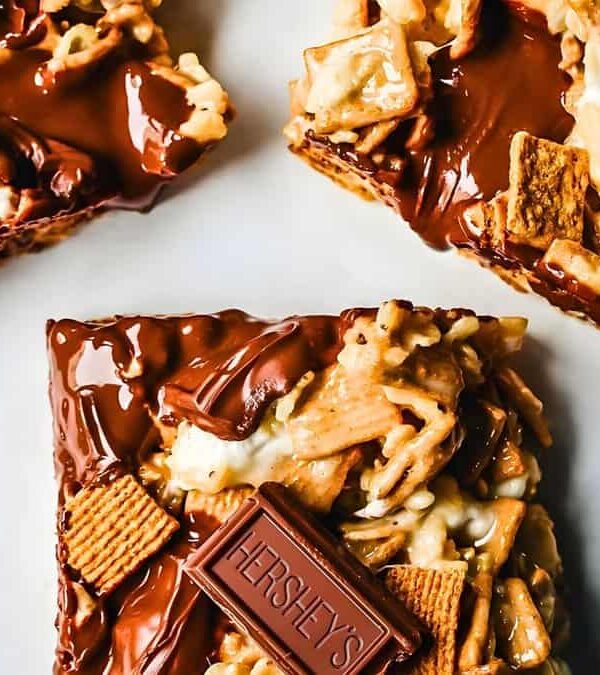 Three chocolate-covered cereal and marshmallow squares topped with small chocolate pieces, arranged on a white surface.