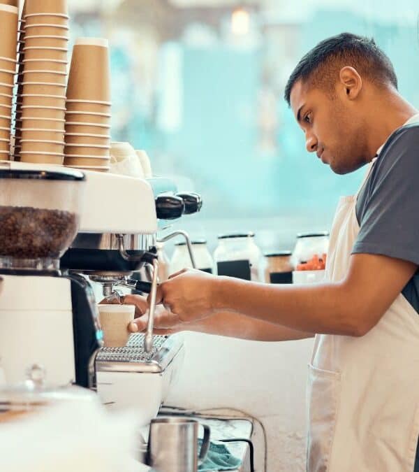 Barista preparing coffee at an espresso machine in a cafe, surrounded by coffee cups and equipment.