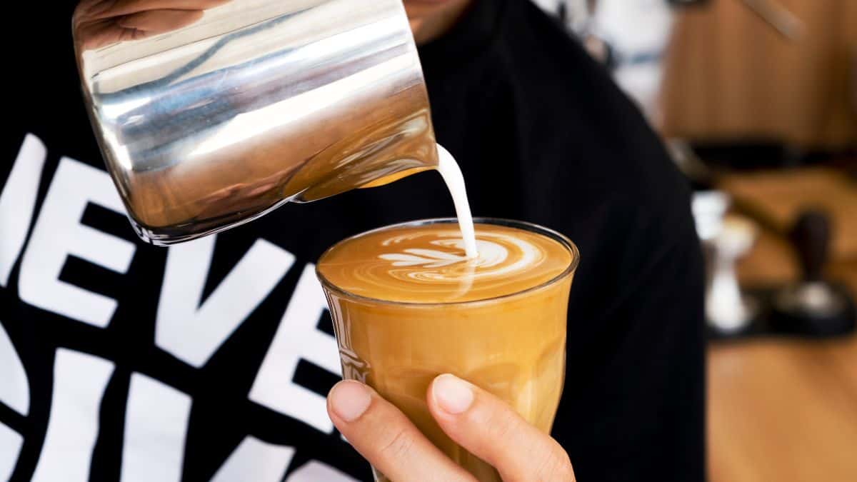A barista pours milk into a coffee cup, creating latte art.