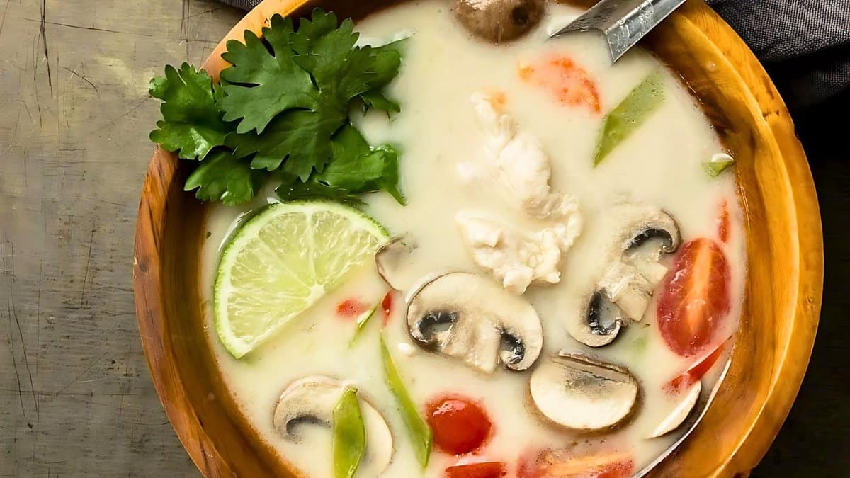 A bowl of Tom Kha Gai soup with chicken, mushrooms, tomatoes, lime, and cilantro in a creamy coconut milk broth.