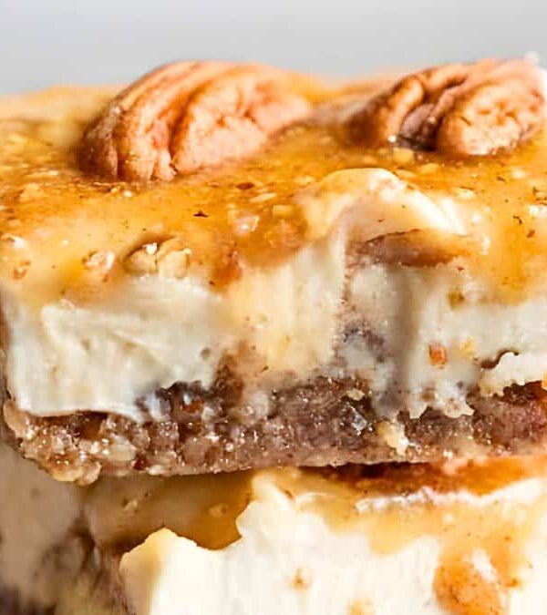 Close-up of a layered dessert bar topped with a pecan, featuring a graham cracker base, creamy filling, and caramel drizzle.