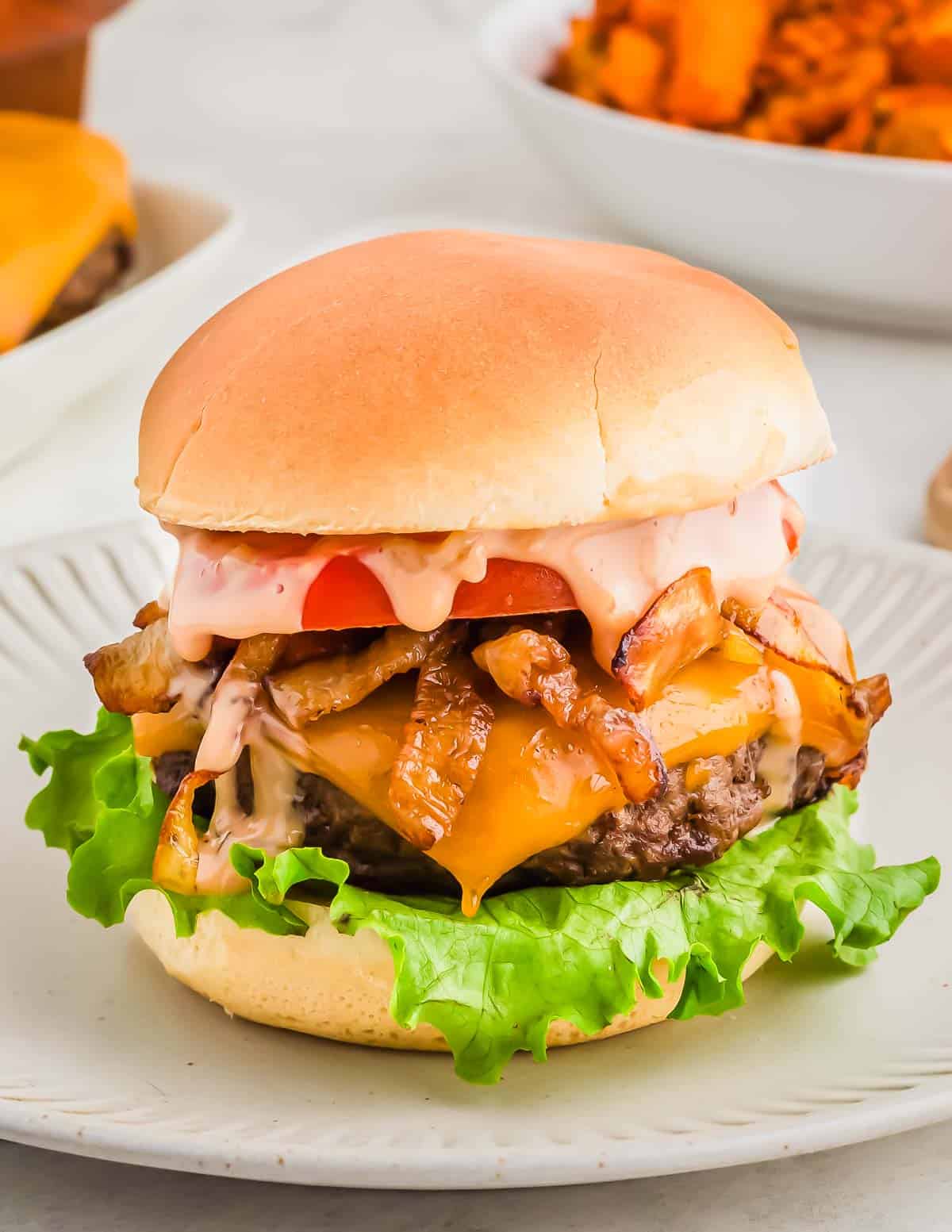 Bison cheeseburger with lettuce, tomato, grilled onions, and sauce on a bun, served on a white plate.