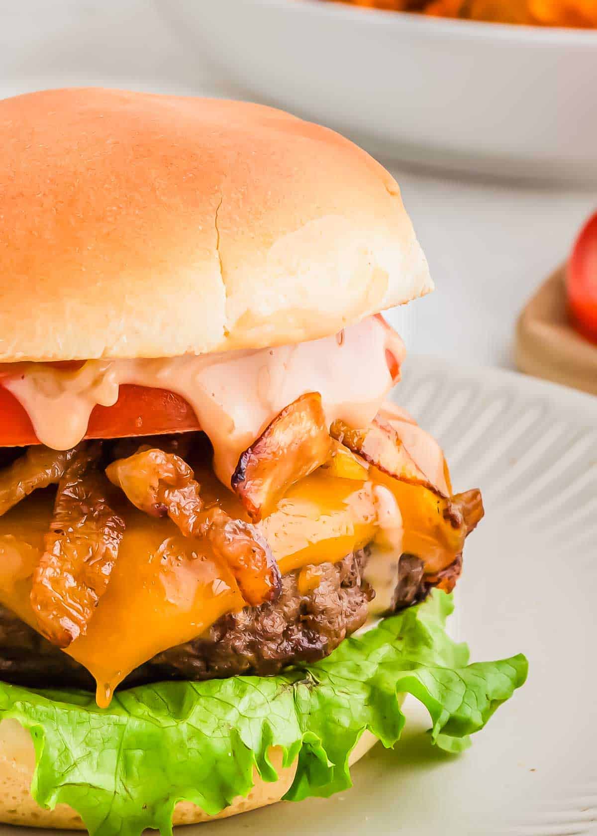 A juicy bison cheeseburger with lettuce, melted cheese, and caramelized onions on a bun, served on a plate with a blurred background.