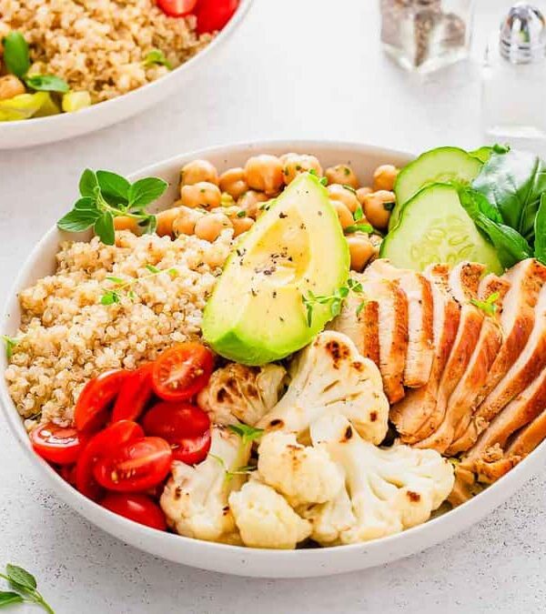 Healthy meal in a bowl with grilled chicken, quinoa, chickpeas, avocado, tomatoes, and cauliflower, garnished with fresh basil.