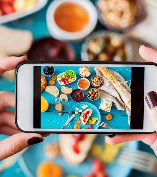 A person takes a photo of a variety of colorful foods arranged on a blue table using a smartphone.