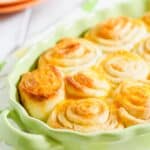 A close-up of freshly baked orange cinnamon rolls in a green ceramic dish.
