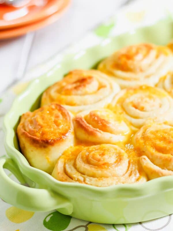 A close-up of freshly baked orange cinnamon rolls in a green ceramic dish.