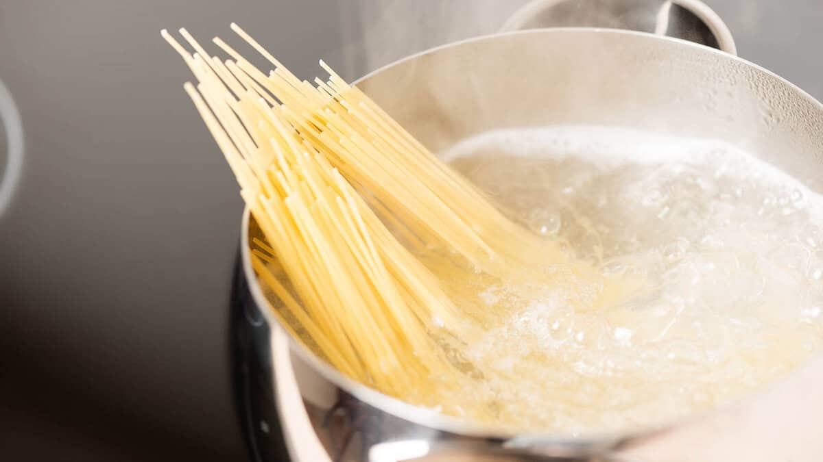 A bundle of spaghetti is boiling in a pot of water on a stovetop.