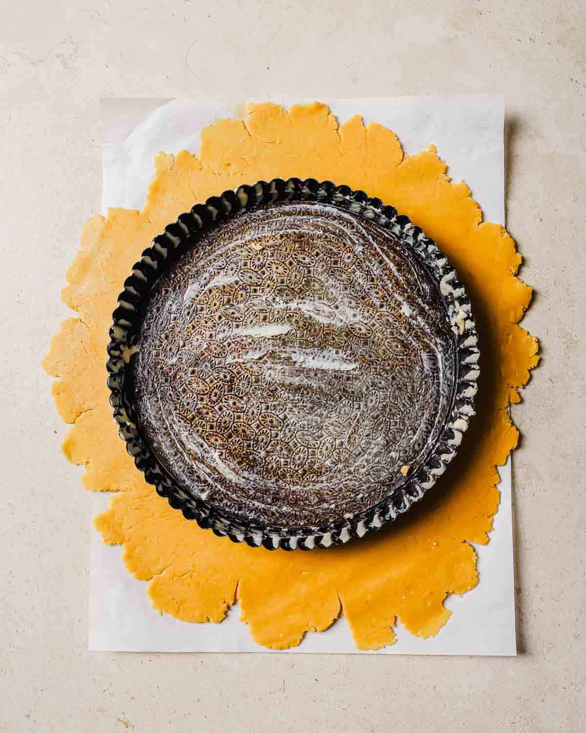 Tart dough with a greased tart pan on top of it.