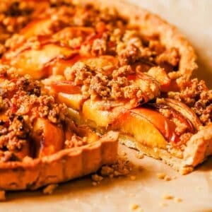 A freshly baked peach tart with a golden crust, topped with sliced peaches and streusel topping, served on parchment paper.