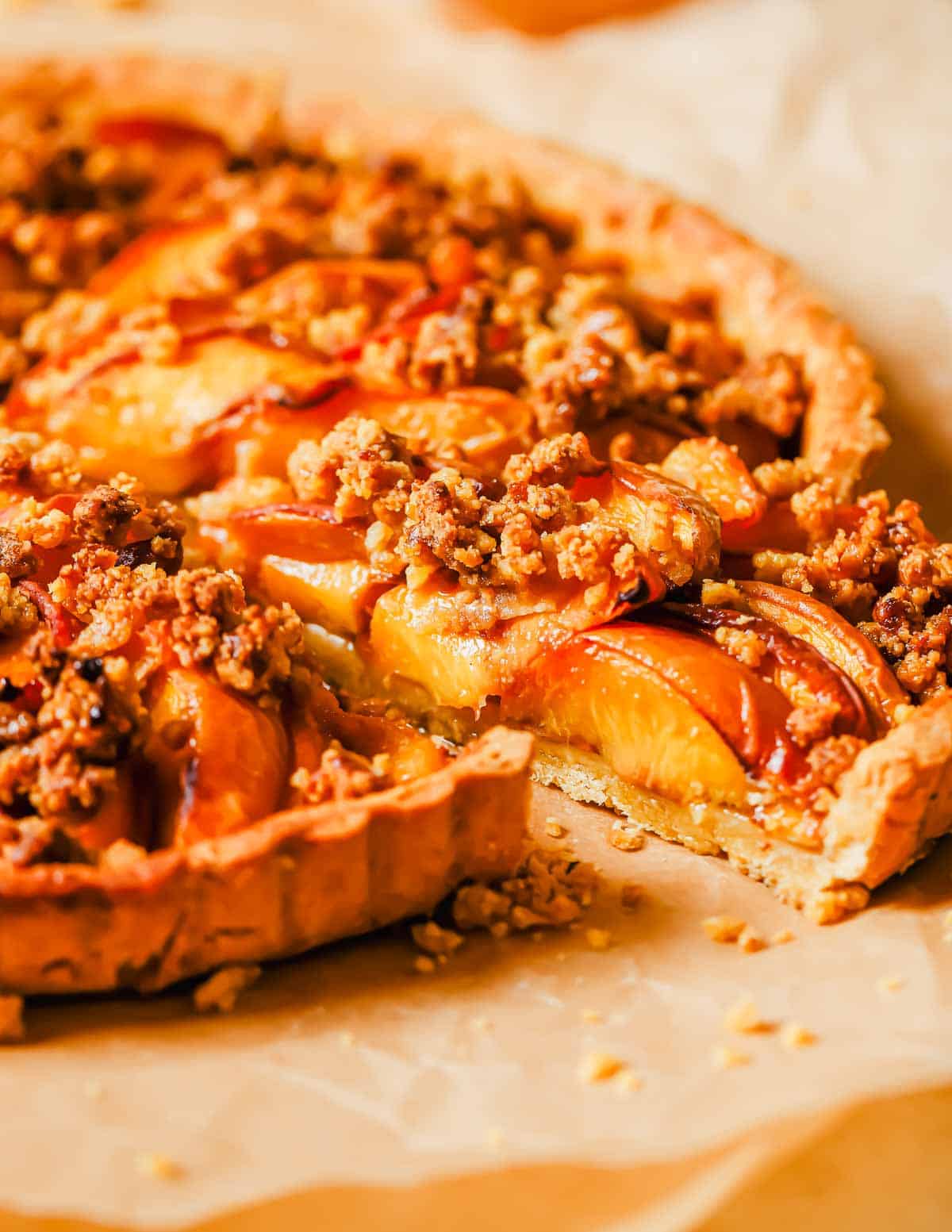 A freshly baked peach tart with a golden crust, topped with sliced peaches and streusel topping, served on parchment paper.