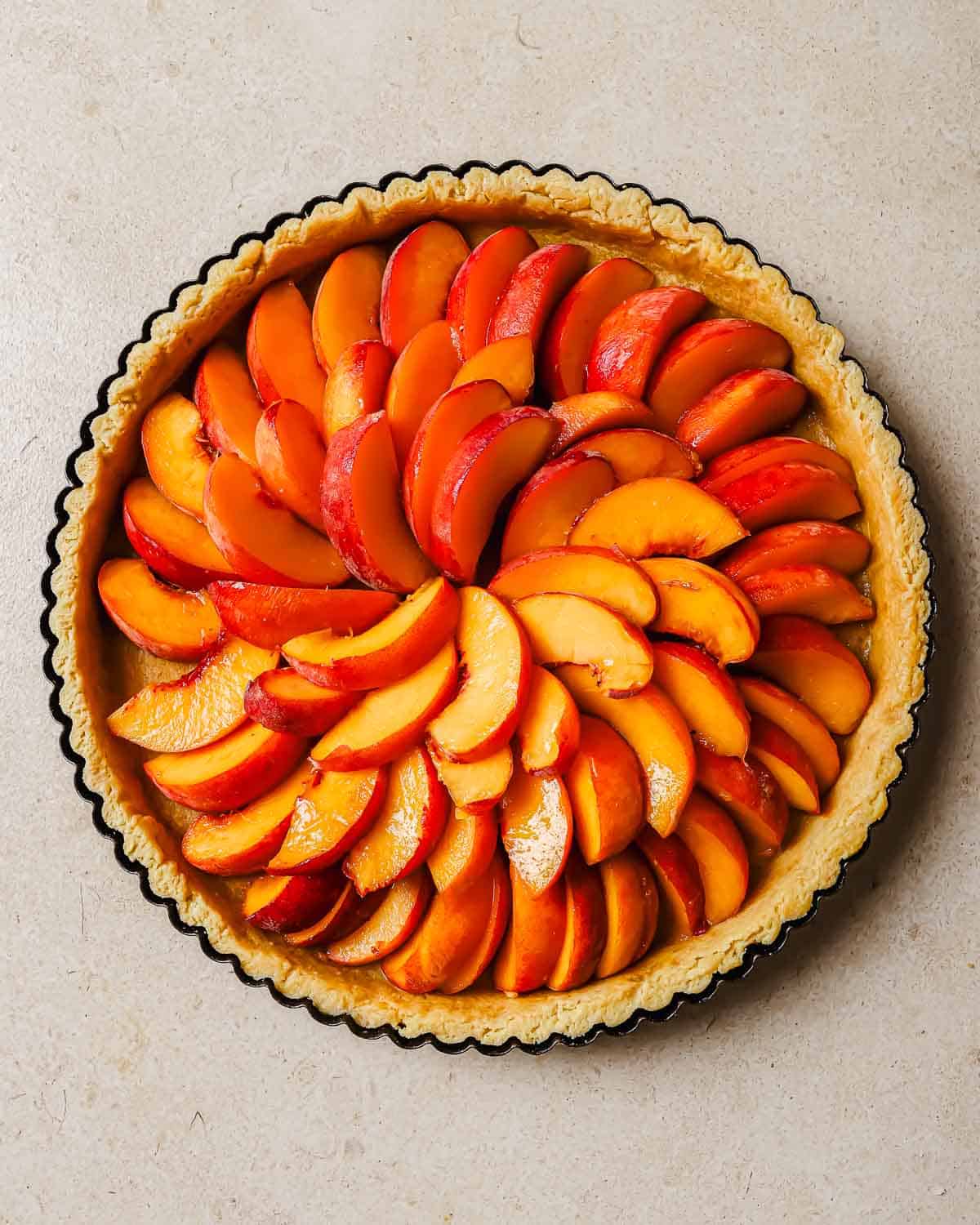 Tart crust with sliced peaches arranged in a circular pattern inside it.