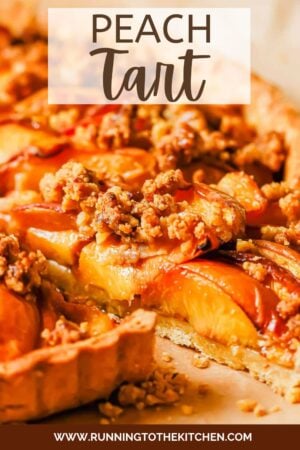 A close-up of a peach tart with a golden crust, topped with sliced peaches and a crumbly streusel, drizzled with caramel.