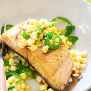A plate of cooked sablefish topped with corn kernels and sliced jalapeños, garnished with parsley. A fork rests on the edge of the plate.
