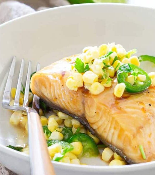 A plate of cooked sablefish topped with corn and sliced jalapeños, accompanied by spinach, with a fork resting on the side.