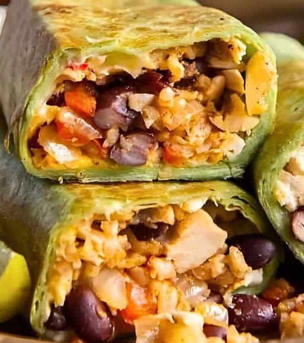 Close-up of a plate with a halved burrito revealing a filling of vegetables, beans, and chicken, next to lemon wedges.