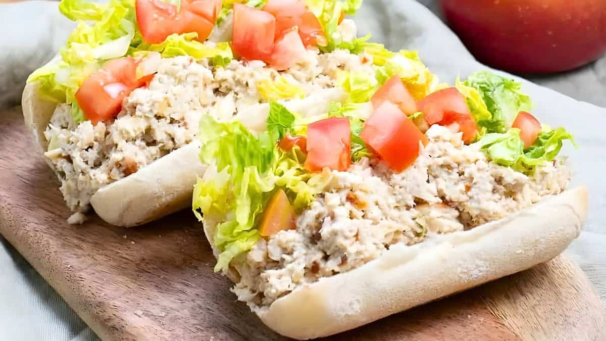 Two hoagie sandwiches filled with chicken salad, topped with shredded lettuce and diced tomatoes, placed on a wooden serving board.