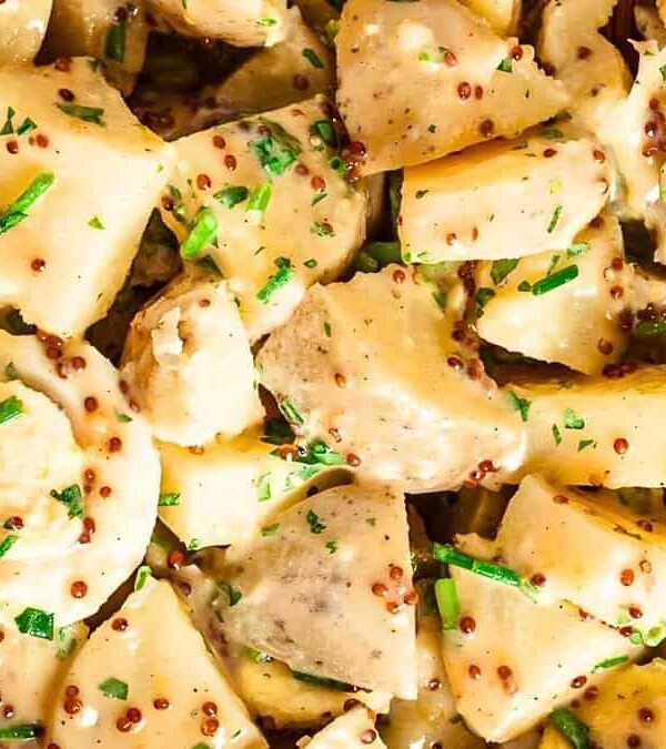 Close-up of a potato salad with mustard seeds, chopped chives, and creamy dressing. The salad is served in a wooden bowl.