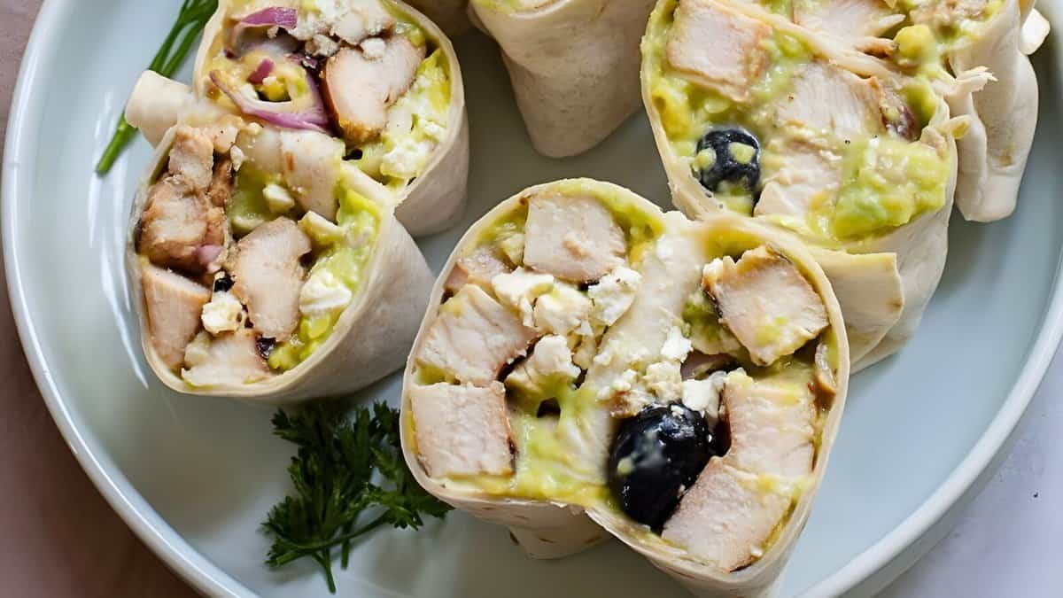 Plate of sliced wraps filled with chicken, guacamole, olives, feta cheese, and red onions, garnished with herbs.