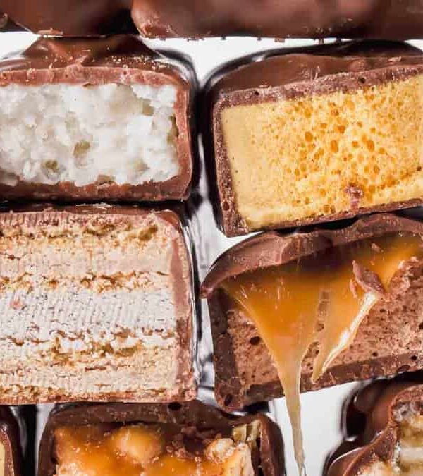 Stack of assorted chocolate-covered candies, showing cross-sections of various fillings including nougat, wafers, caramel, and crispy rice.