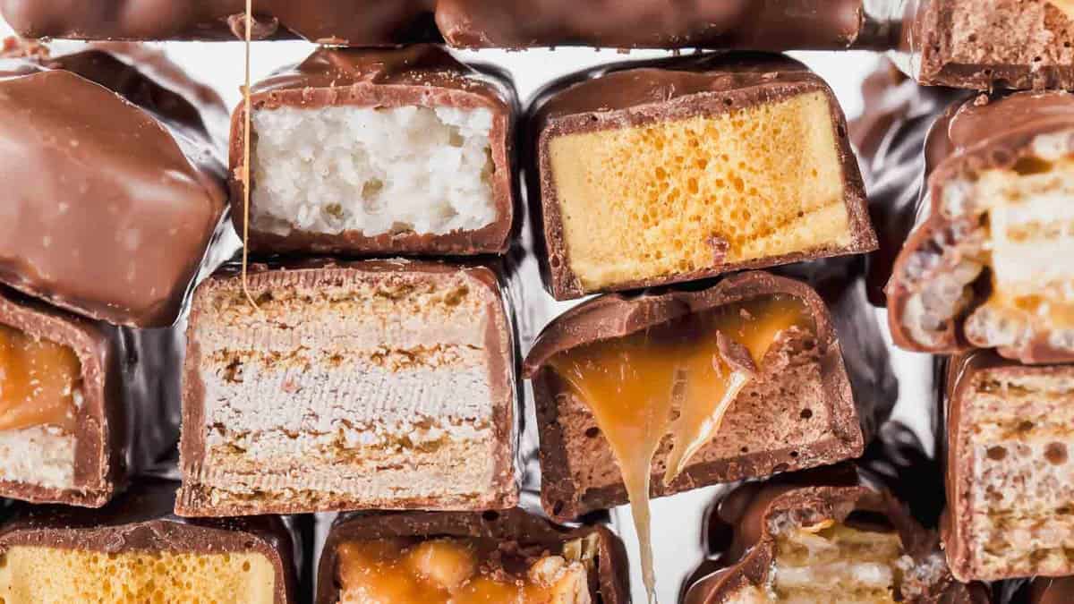 Stack of assorted chocolate-covered candies, showing cross-sections of various fillings including nougat, wafers, caramel, and crispy rice.