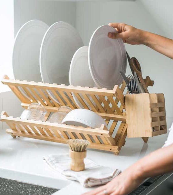 Woman washing dishes in kitchen using eco friendly brush and drying rack.