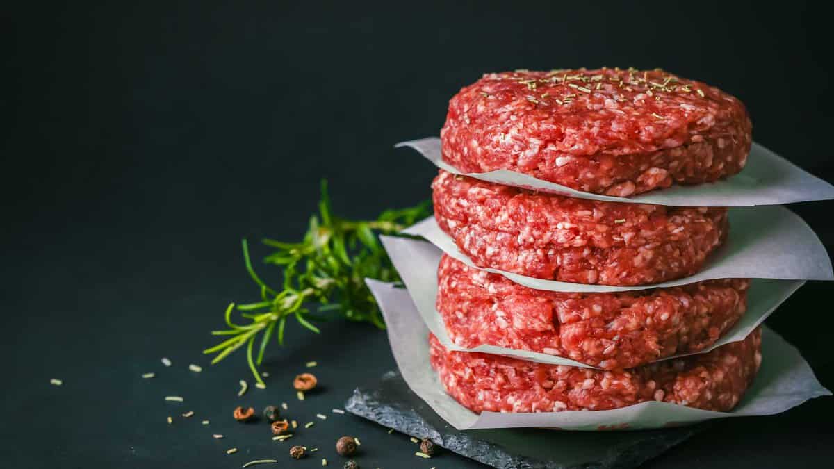 Raw burger patties stacked between parchment paper.