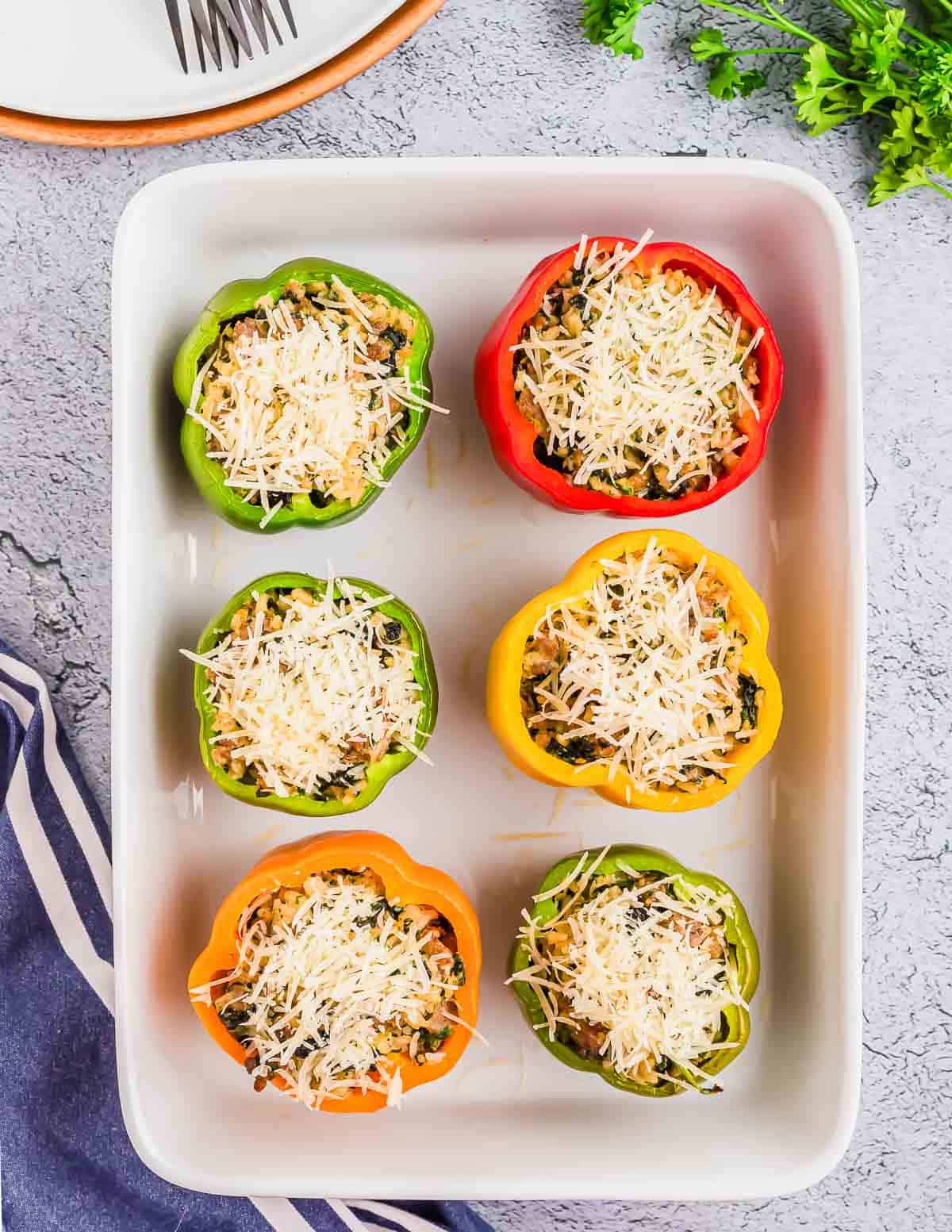 A baking dish contains six stuffed bell peppers, two red, two yellow, and two green, all topped with shredded cheese.