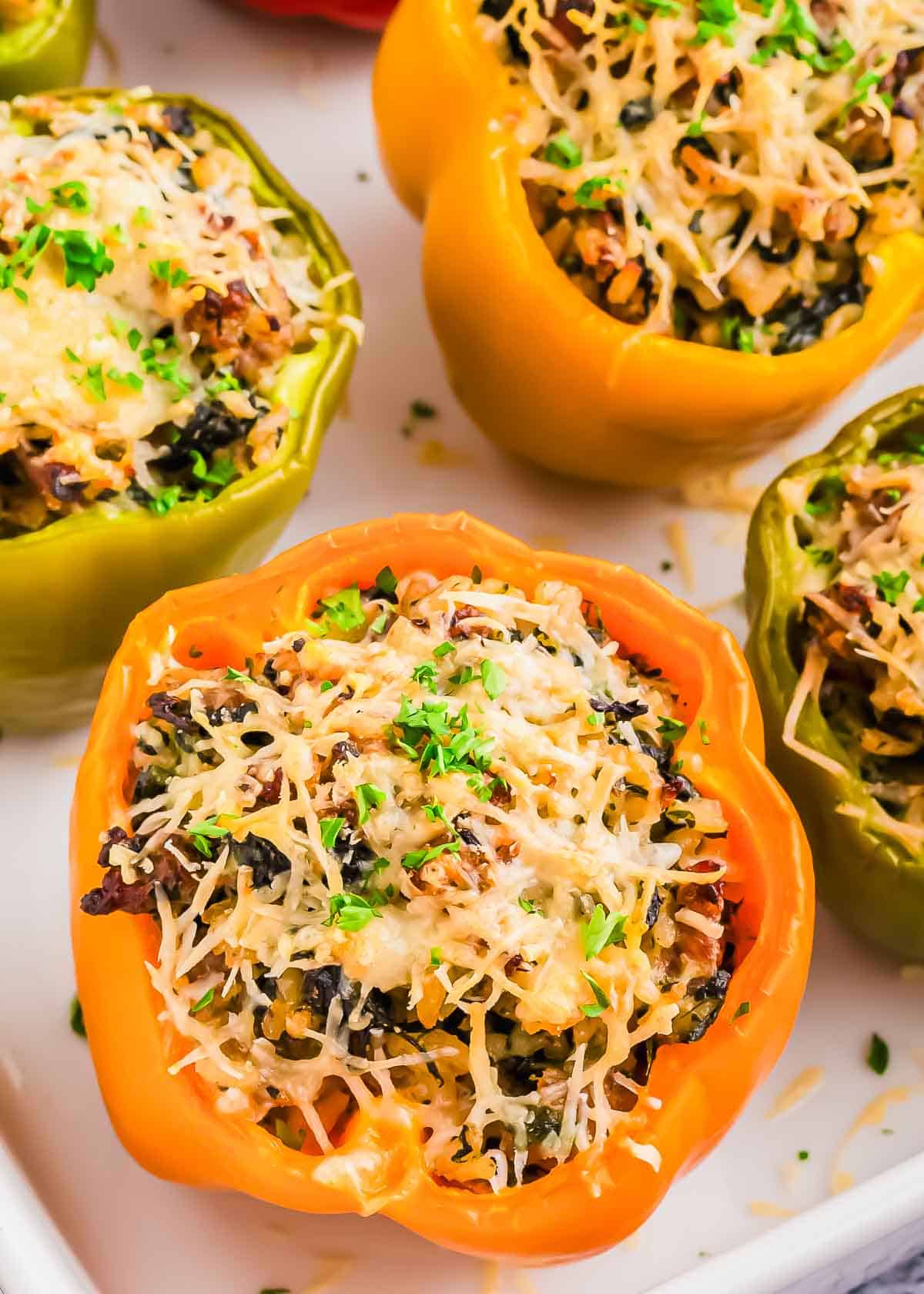 Close-up of colorful stuffed bell peppers filled with rice, vegetables, and topped with melted cheese and herbs on a white surface.